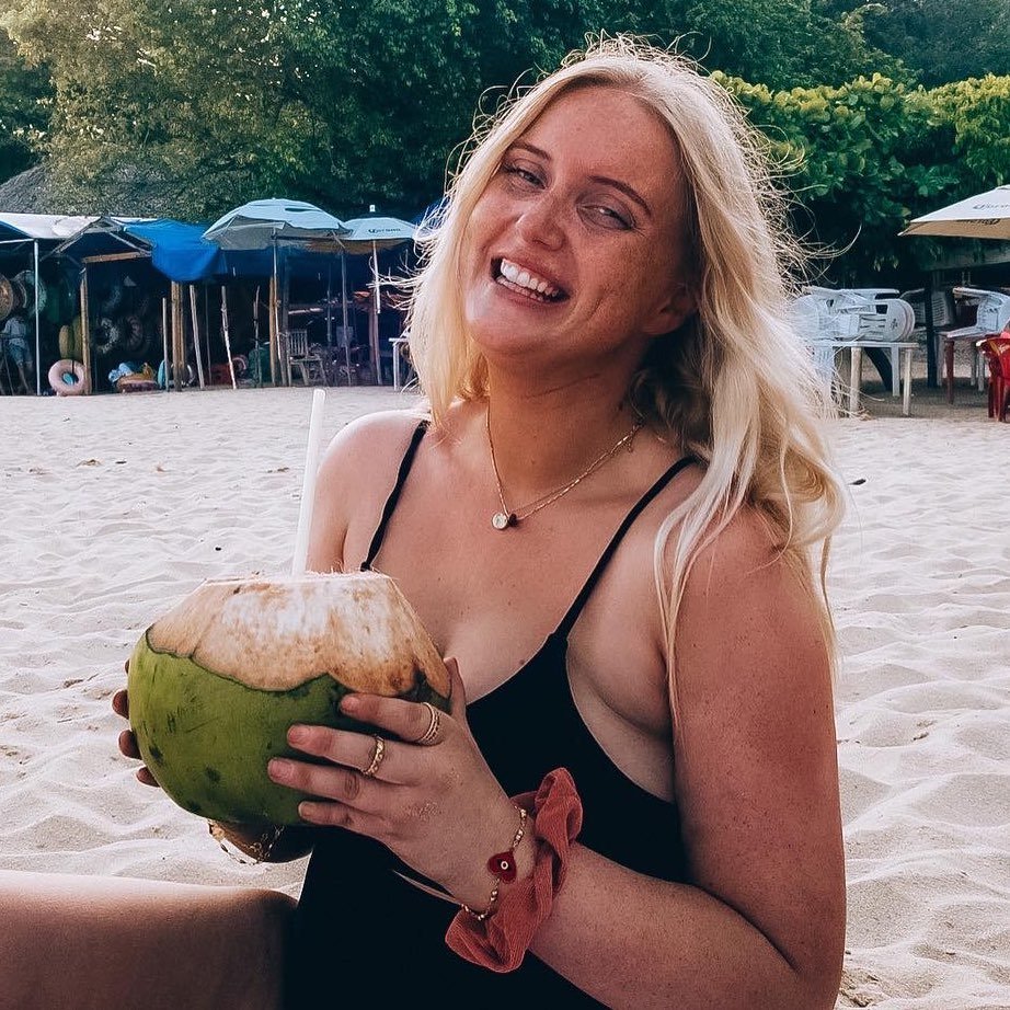 blonde woman influencer on the beach smiling and drinking a coconut