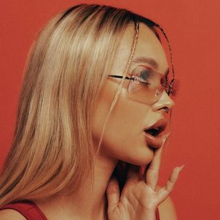 A woman in glasses is posing with her hand on her face.