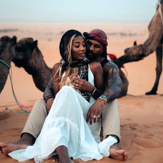 A man and woman sitting in front of camels in the desert.