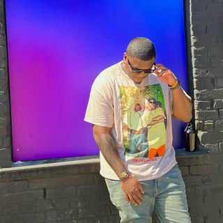 A man leaning against a wall wearing a t - shirt.