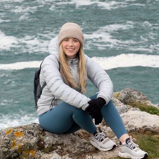 Blonde Travel Influencer sitting on a rock before the agitated sea.