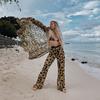 A woman is standing on the beach in leopard print pants.