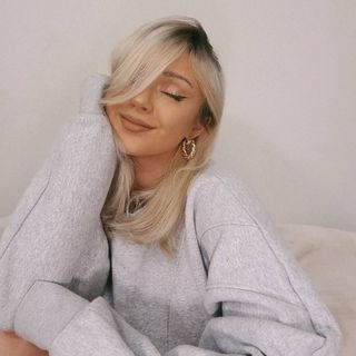 A woman in a grey sweatshirt posing on a couch.