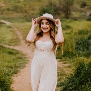 A woman in a white jumpsuit standing on a dirt path.