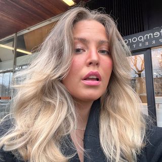 A woman with long blonde hair is standing in front of a store.