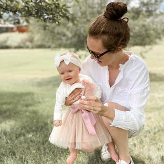 A woman kneeling down with a baby in a pink tulle dress.