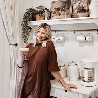 A woman standing in front of a kitchen with a cup of coffee.