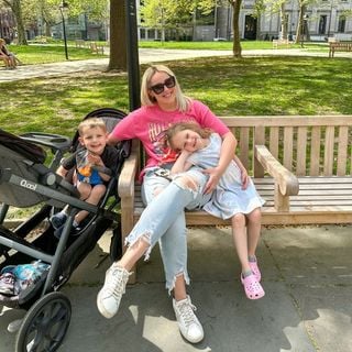 A woman sits on a bench with two children and a stroller.