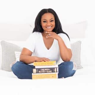 A woman sitting on a bed with a stack of books.