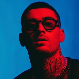 A man with tattoos and glasses in front of a blue background.