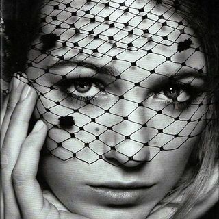 A black and white photo of a woman wearing a net veil.