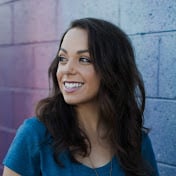 A woman smiling in front of a colorful wall.