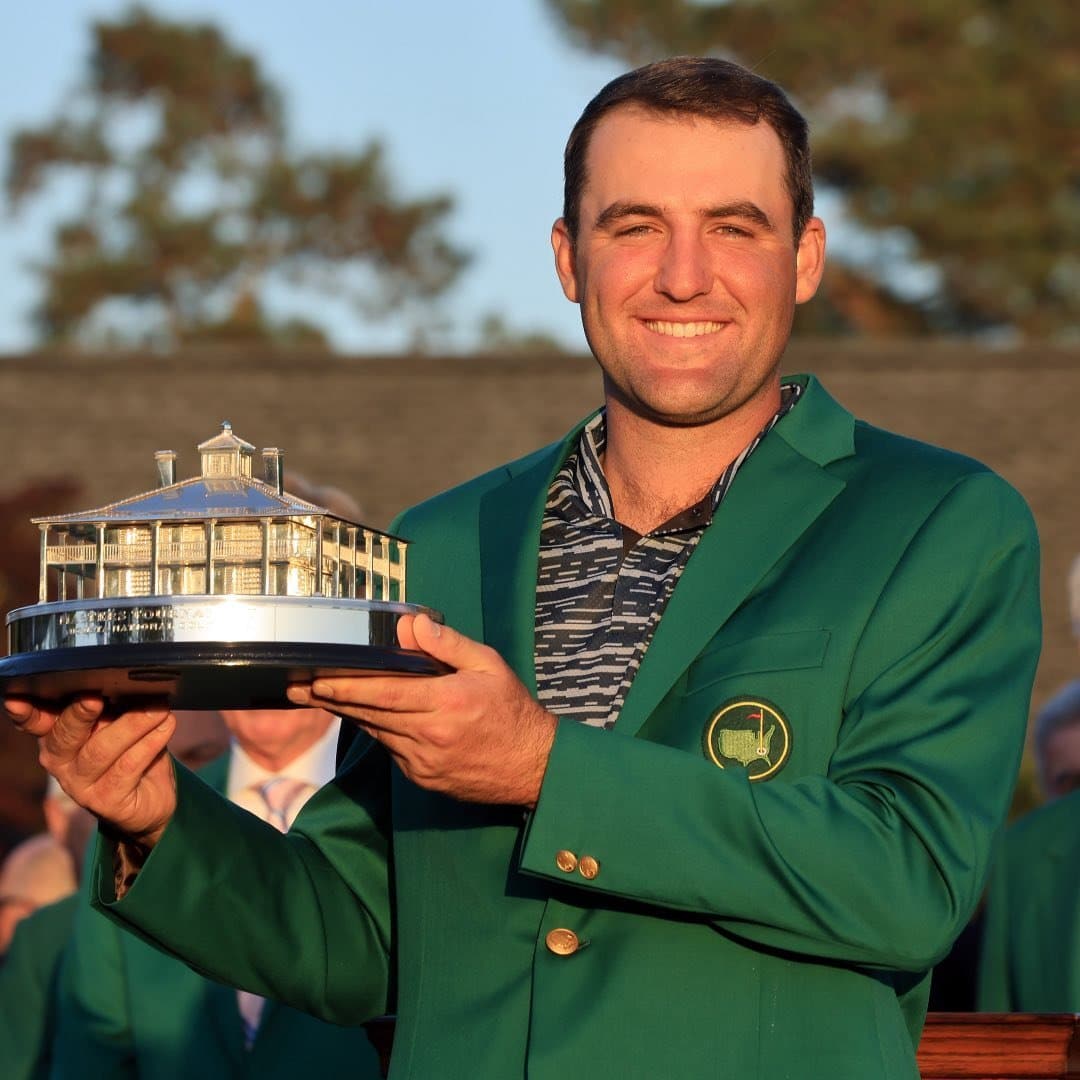 A man in a green jacket holding a trophy.