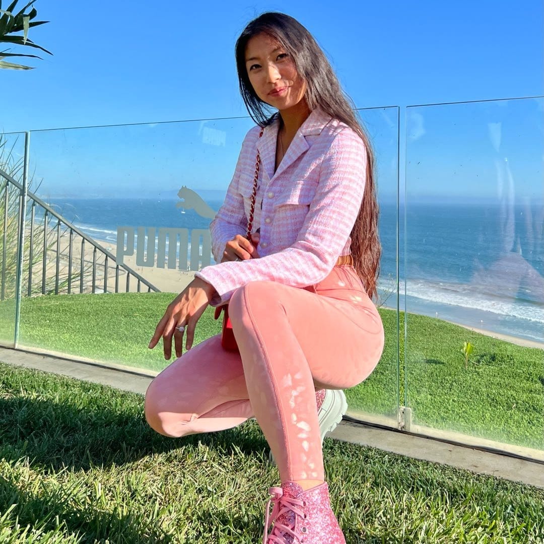 A woman squatting on the grass wearing pink leggings.