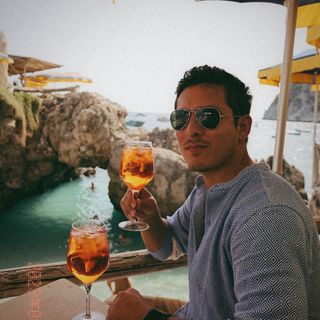 A man holding a glass of wine while sitting on a beach.