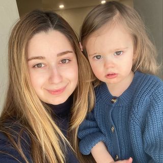 A woman is holding a little girl in a blue sweater.