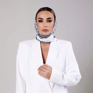 A woman wearing a white blazer and white scarf.