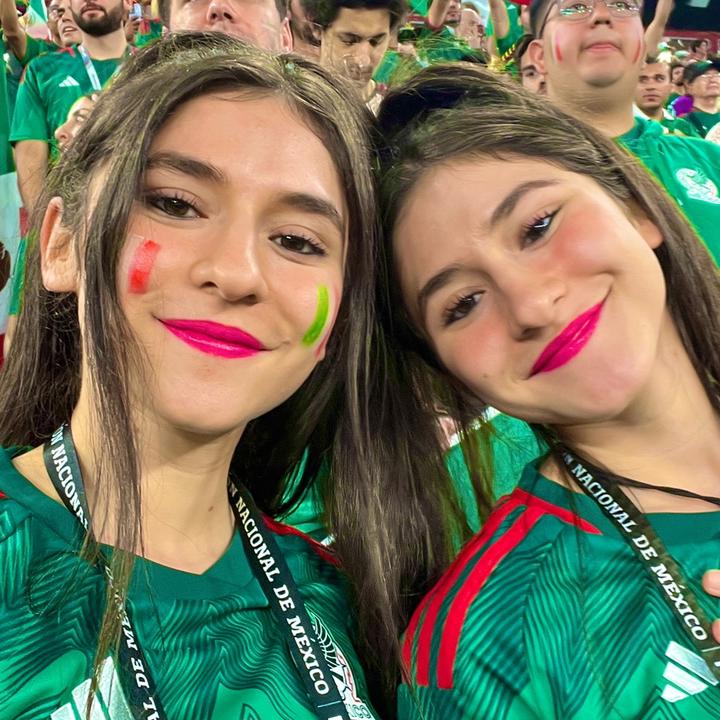 Two mexican girls posing for a photo at a soccer game.