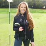 A young woman posing with a golf club on a golf course.