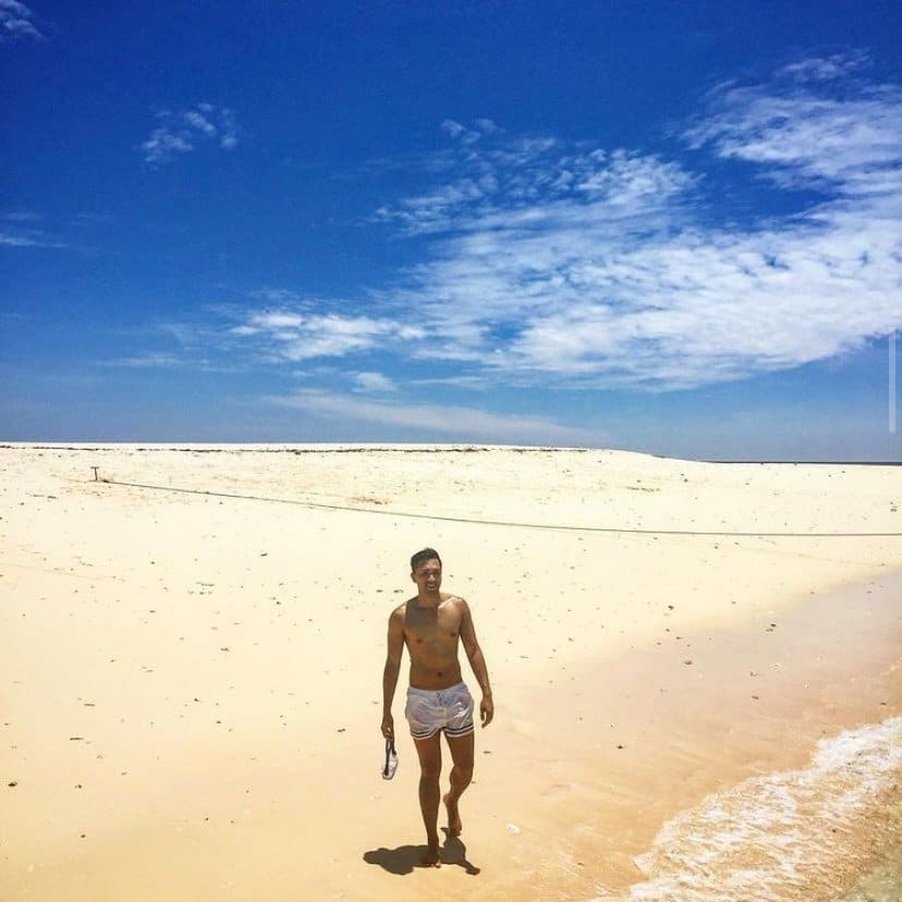 A man in shorts walking on a sandy beach.