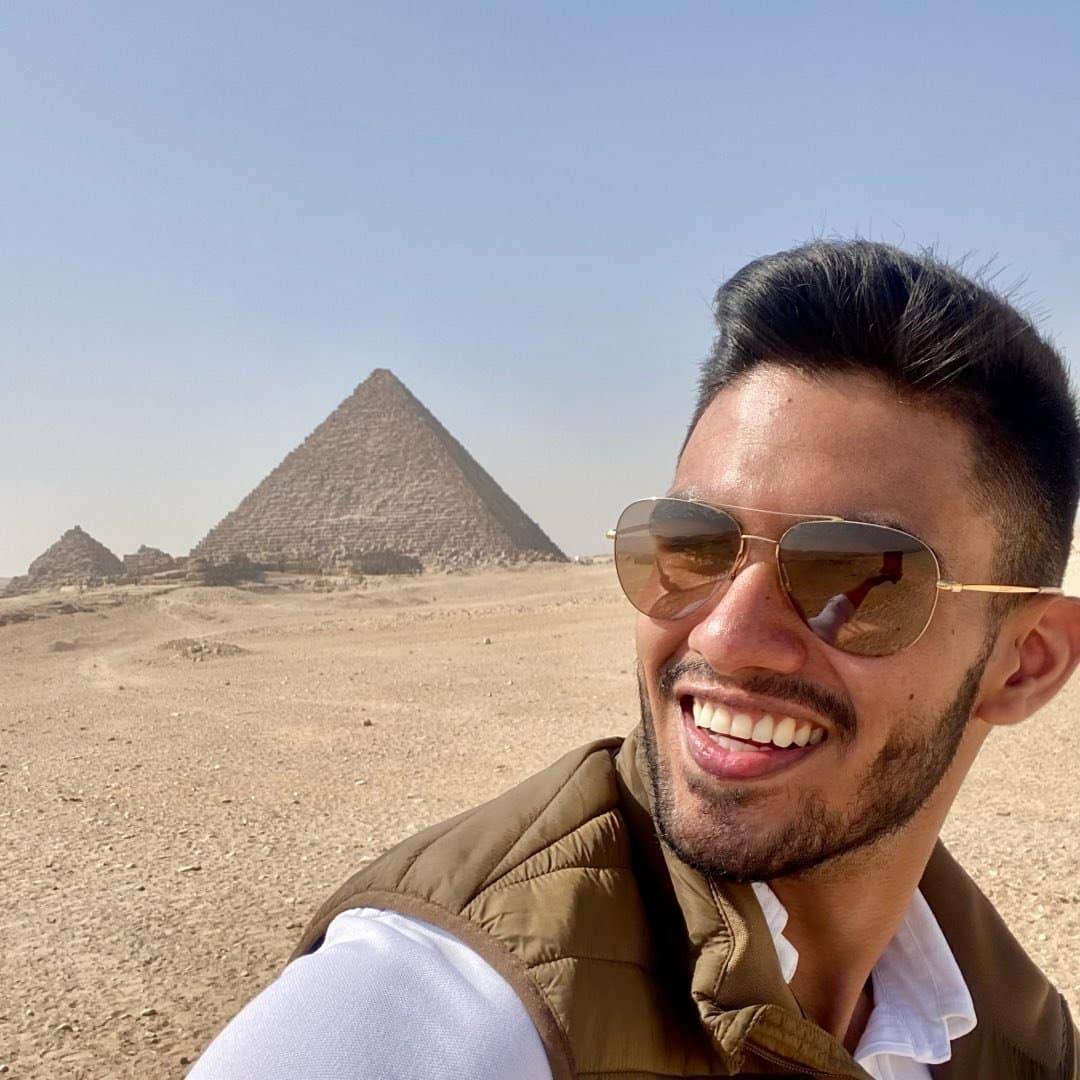 A man is smiling in front of the pyramids in egypt.