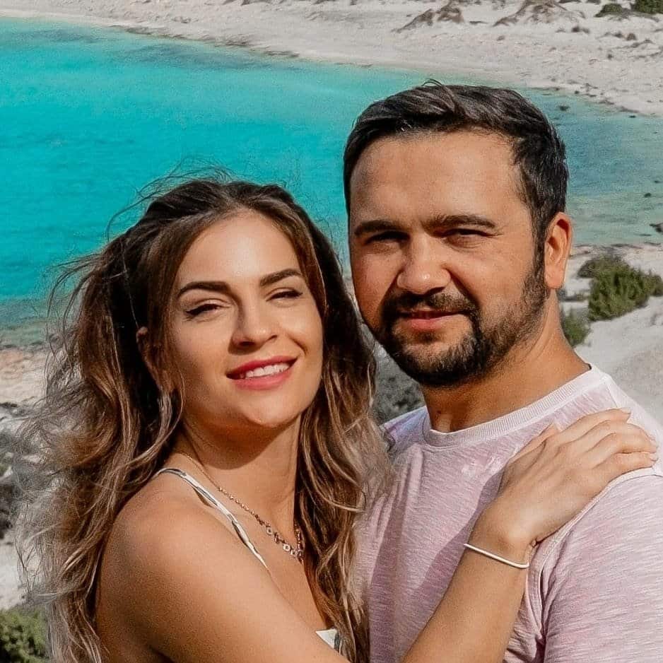 A man and woman posing for a picture in front of a blue sea.