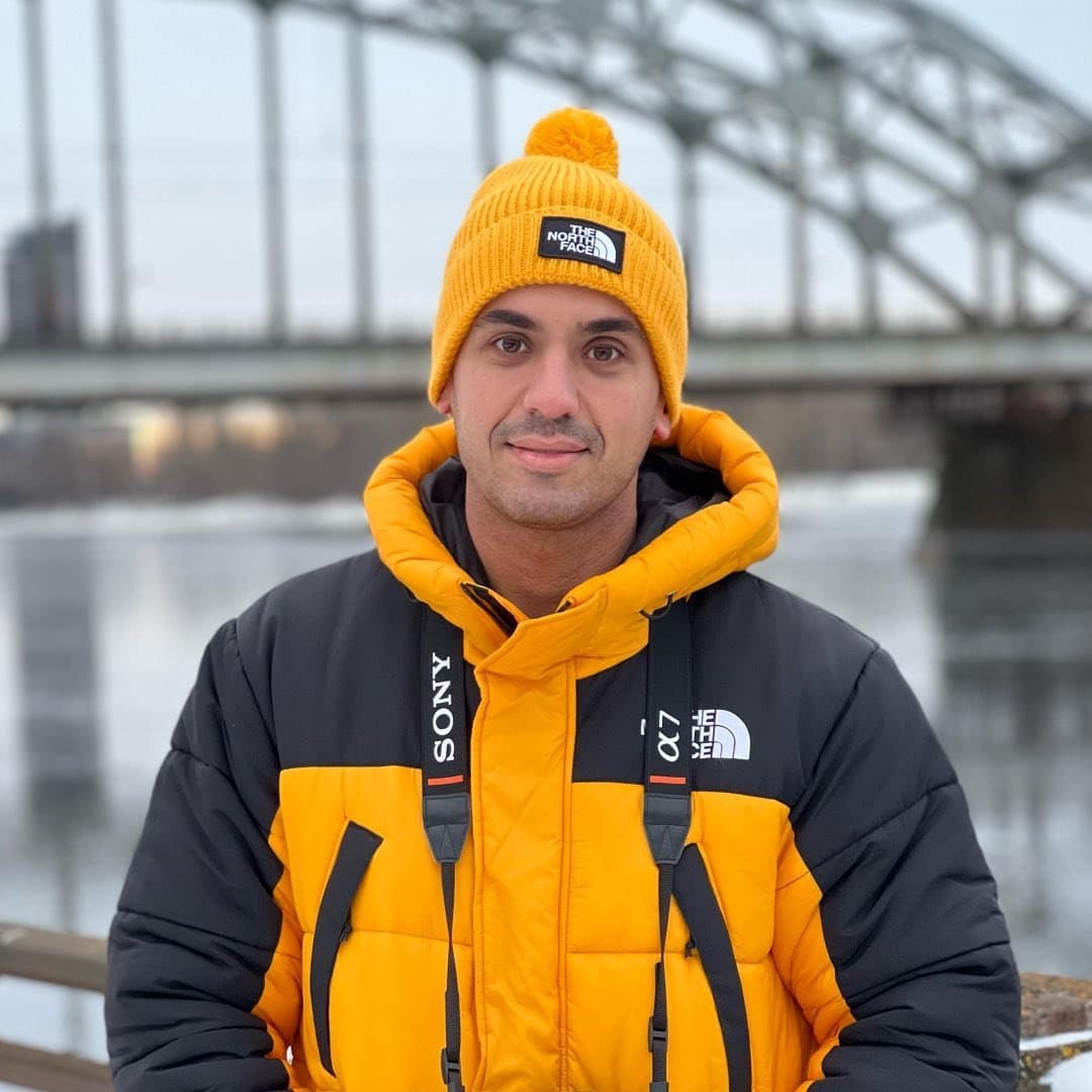 A man in a yellow jacket standing in front of a bridge.