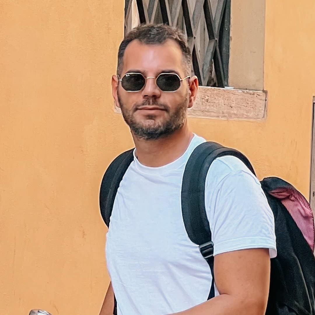 A man with a backpack and sunglasses walking down a street.