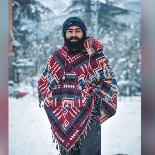 A man in a colorful poncho standing in the snow.