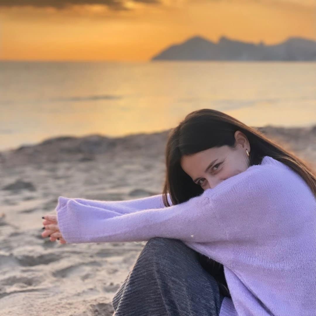 A woman sitting on the beach at sunset.