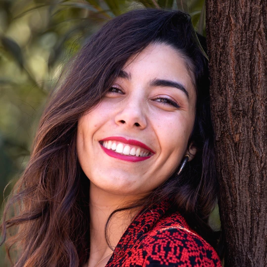 A smiling woman leaning against a tree.