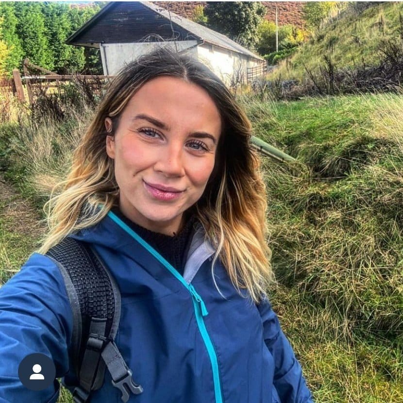 A woman in a blue jacket is taking a selfie in a field.