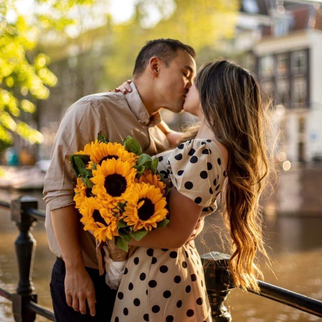 A couple kissing in front of a canal with sunflowers.