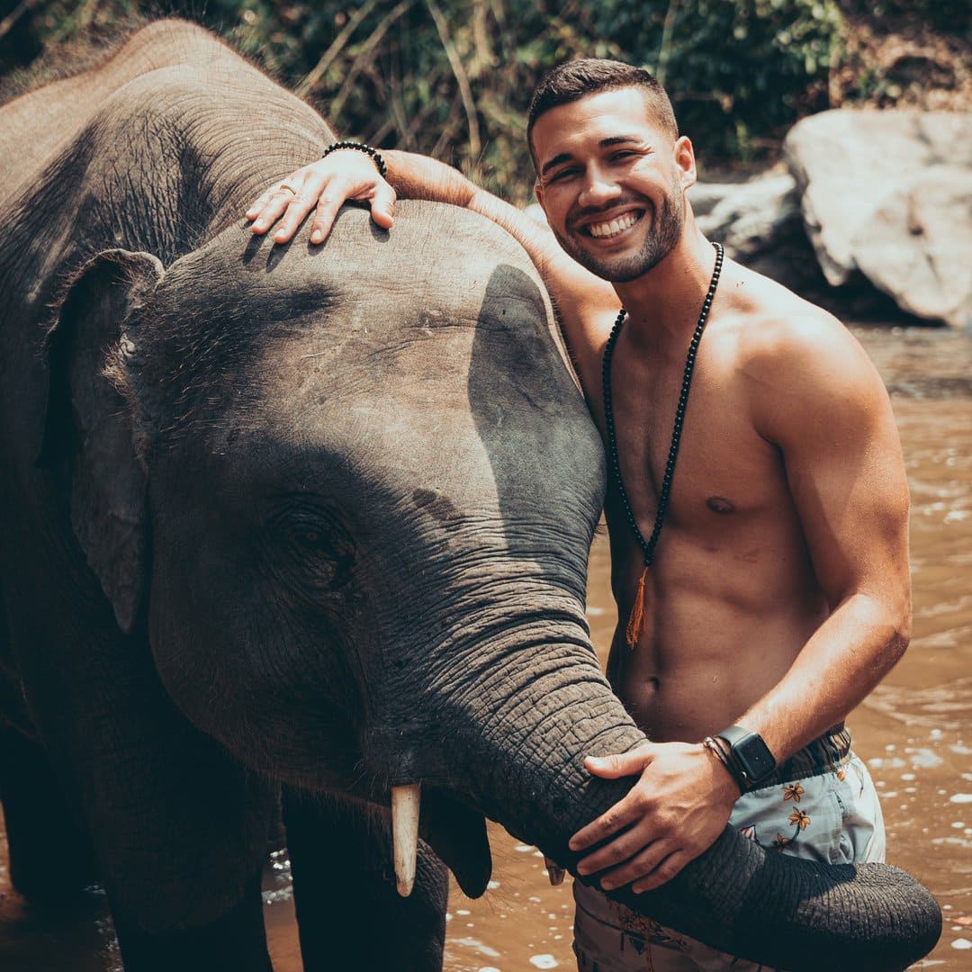 A shirtless man is hugging an elephant.