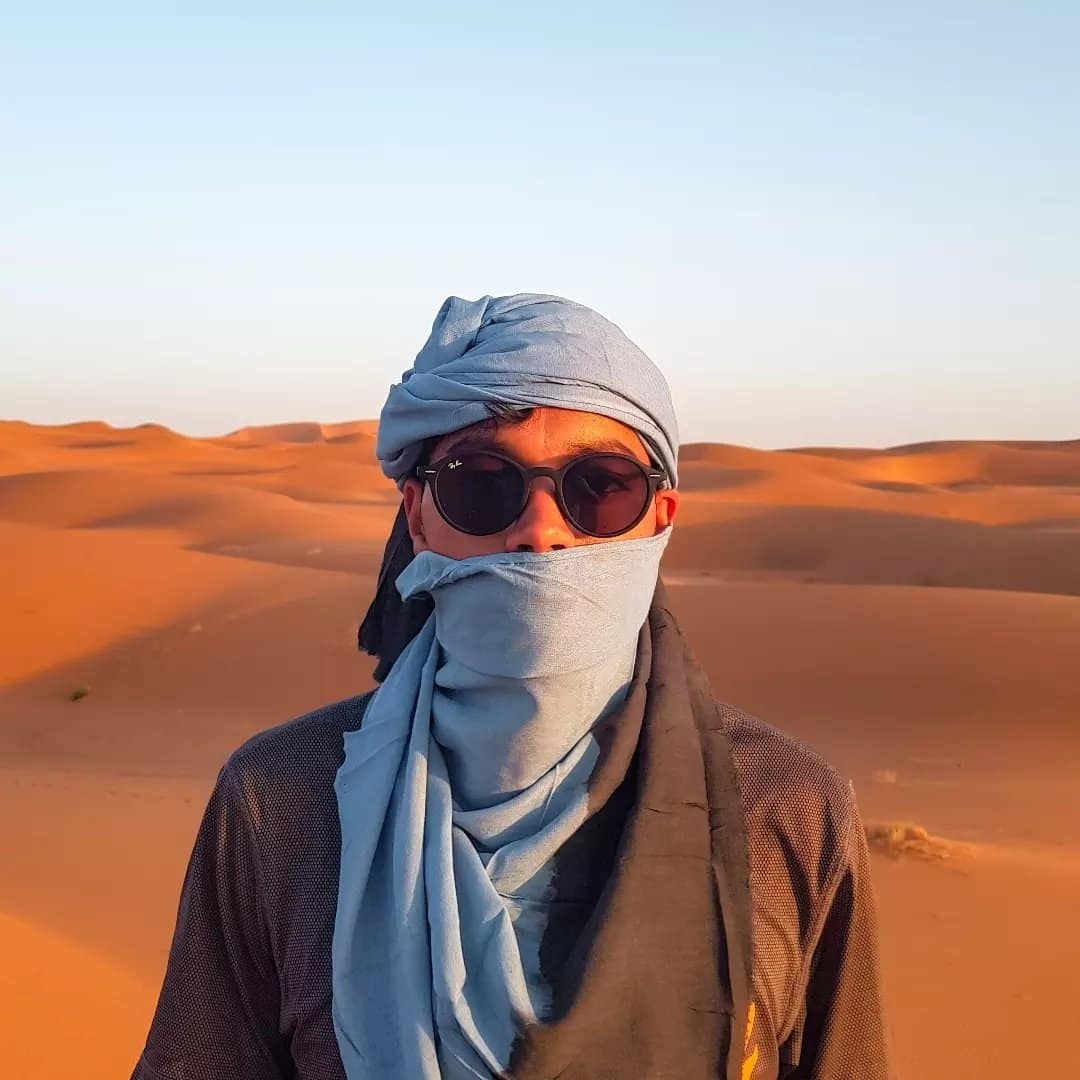 A man wearing a scarf and sunglasses in the sahara desert.
