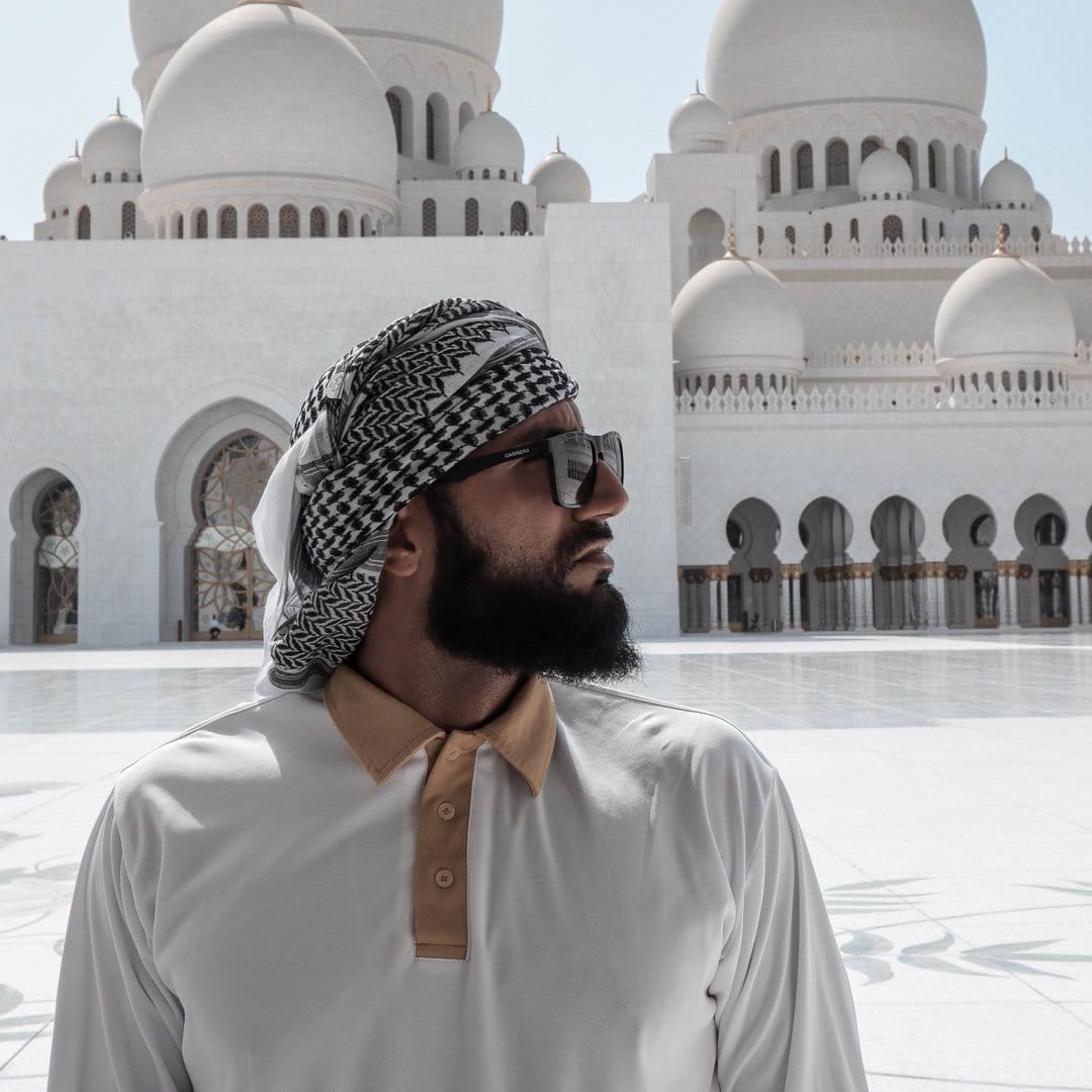 A man in a turban standing in front of a white mosque.