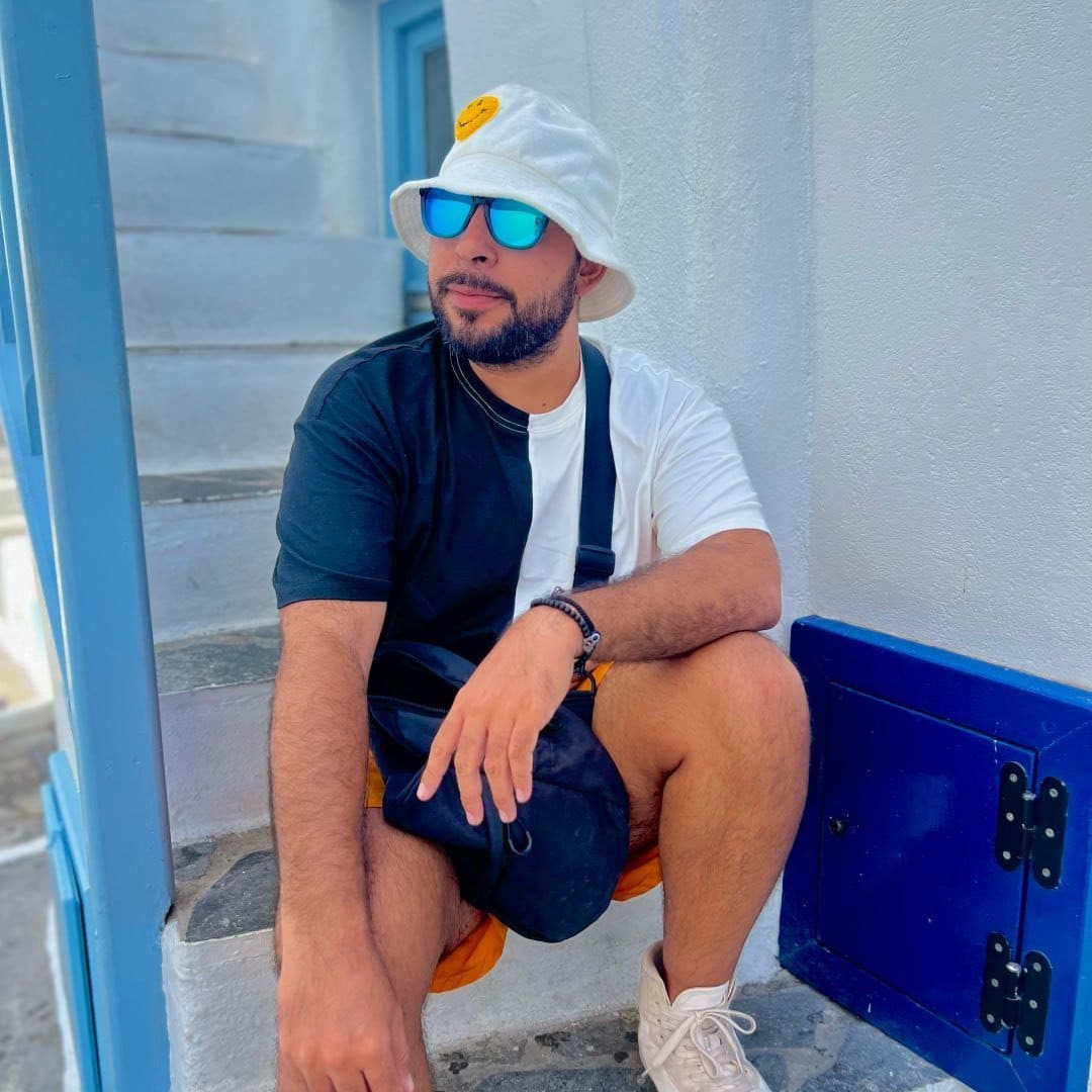 A man sitting on steps wearing a hat and sunglasses.