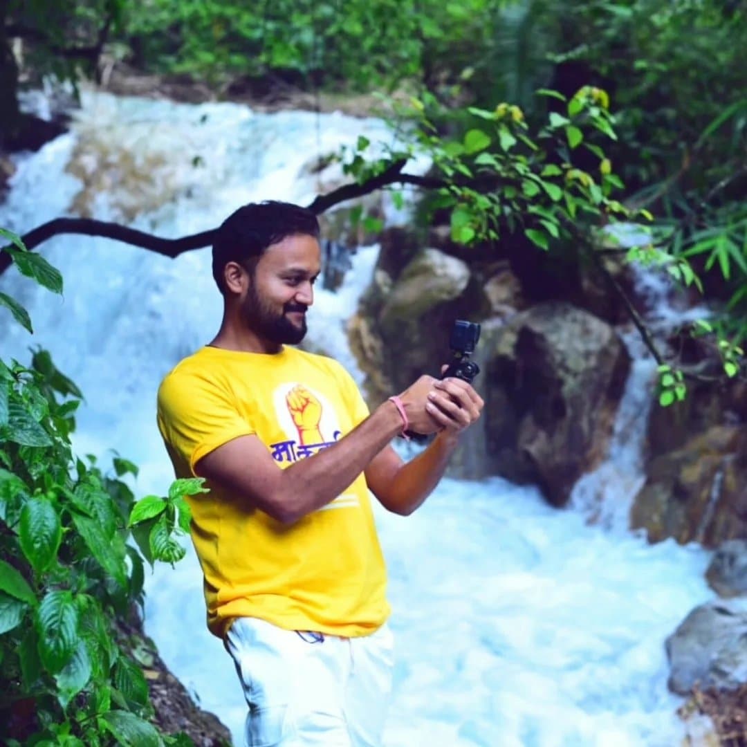 A man in a yellow t - shirt taking a picture of a waterfall.