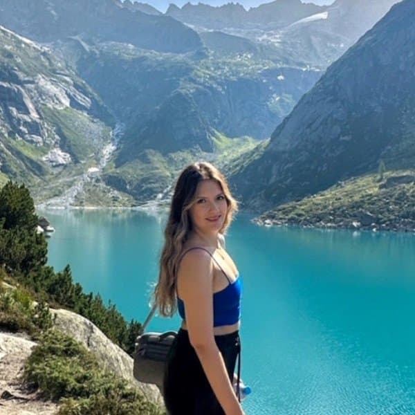 A woman standing in front of a mountain with a blue lake in the background.