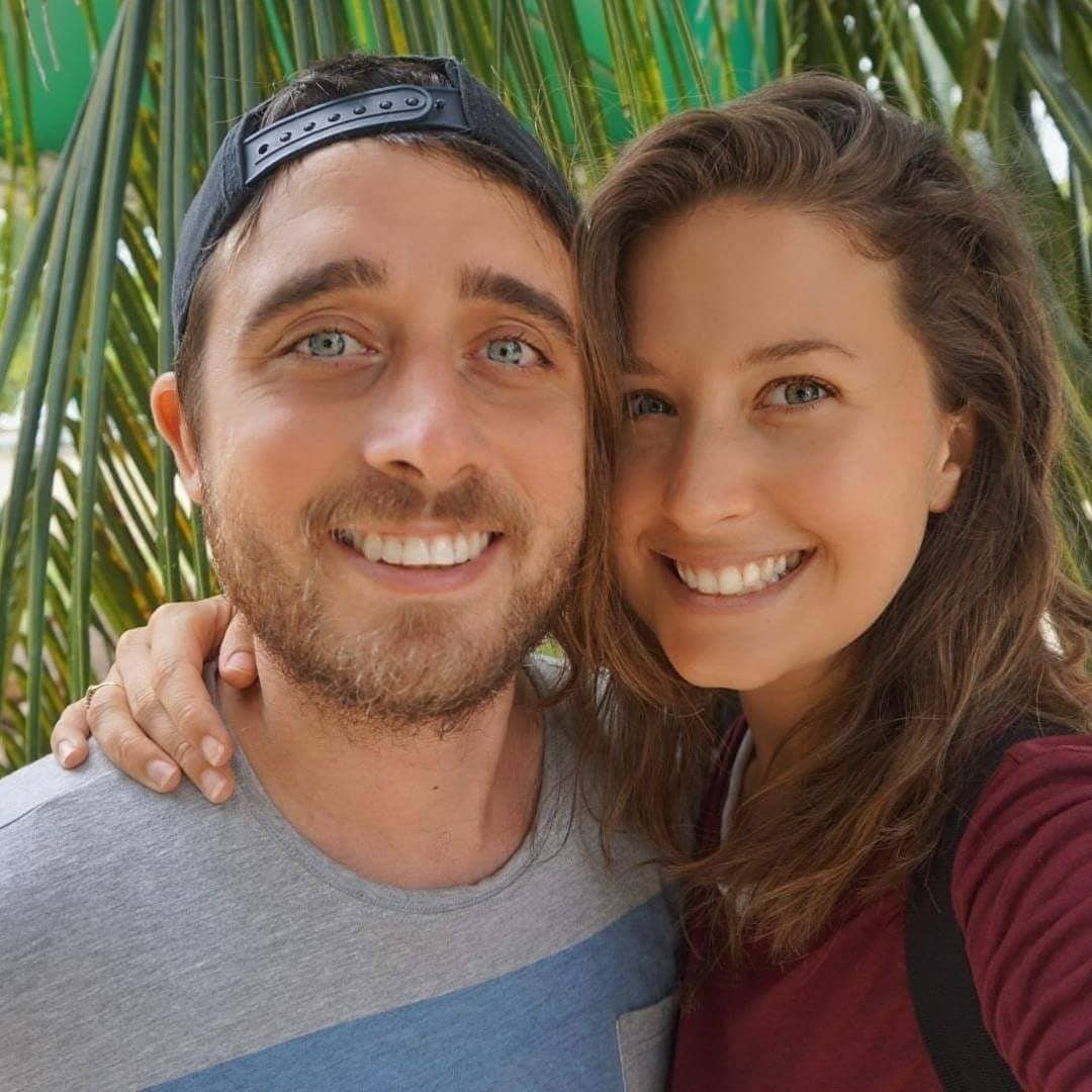 A man and woman smiling in front of a palm tree.