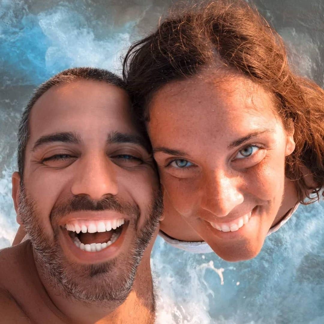 A man and woman taking a selfie in the ocean.