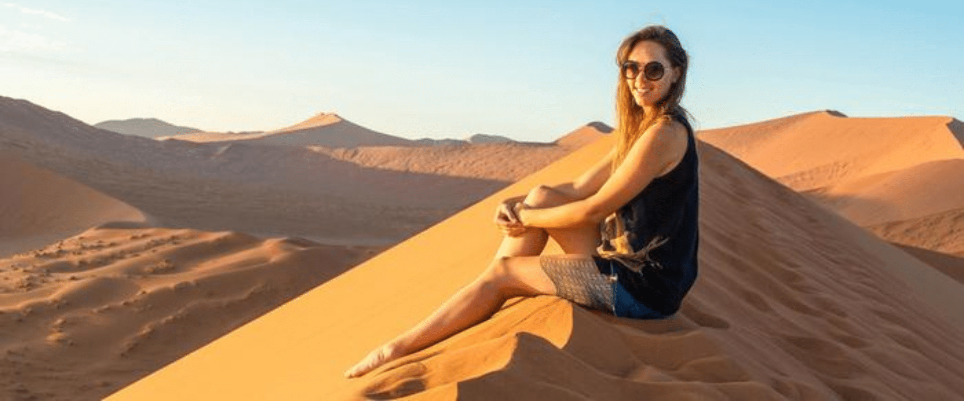A woman sitting on top of a sand dune in the desert.