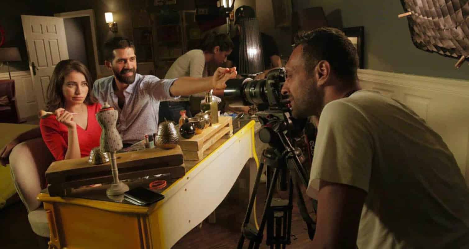 A man and a woman are filming a scene in a room.