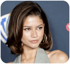 Influencer Profil - V.2 1 Eine Frau mit schulterlangen braunen Haaren und Ohrringen posiert vor einem dunkelblauen Hintergrund mit Logos und trägt ein ärmelloses graues Oberteil.