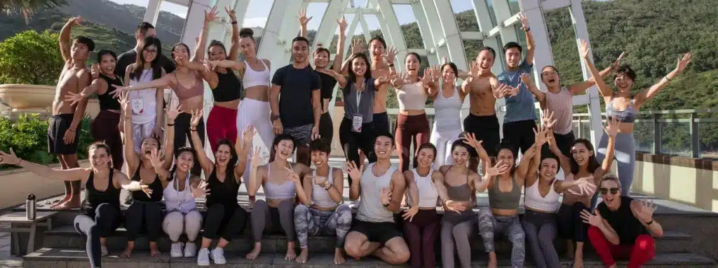 What Is Brand Advocacy? (7 Top Brand Programs Explained) 24 A large group of people in athletic wear pose energetically with arms outstretched on outdoor steps, promoting brand advocacy amid greenery and striking glass architecture in the background.